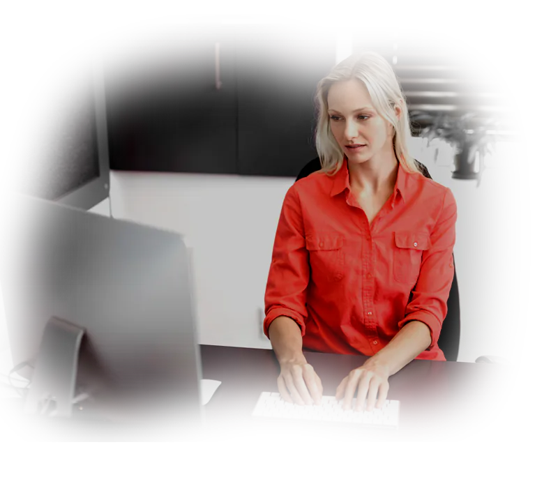 Focused blonde woman in a red shirt working at a computer, representing why premium quality custom web design and pixel-perfect architecture are vital.