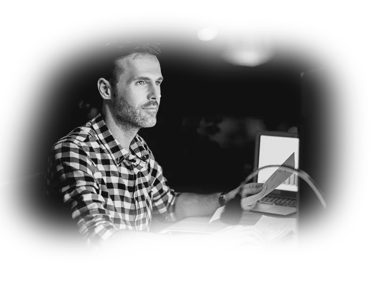 Monochrome photography of a focused web engineer analyzing documents at night, representing custom web engineering for global reach.